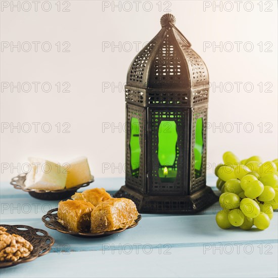 Lantern near green grape with baklava turkish delights saucers