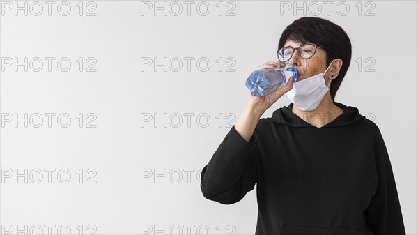 Woman with medical mask drinking water from bottle