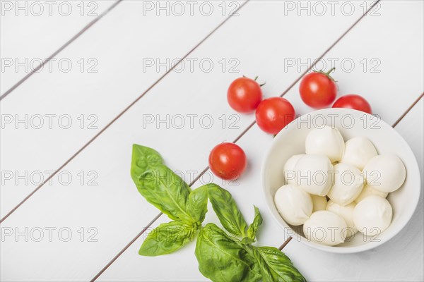 Mozzarella cheese ball with basil leaf red tomatoes wooden white background