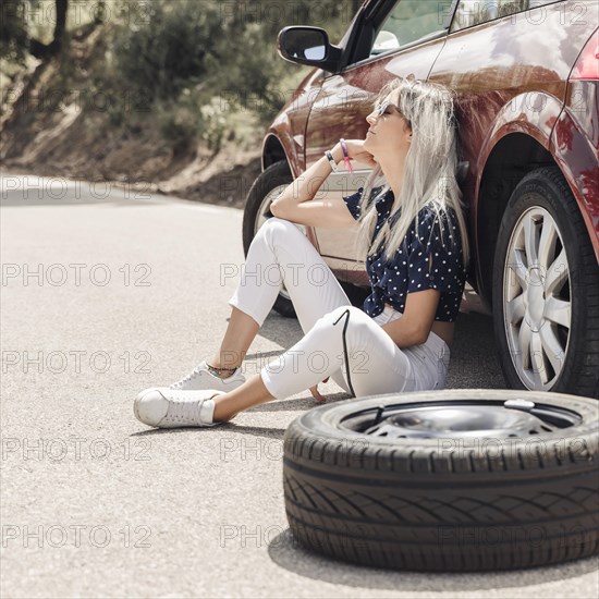 Sad young woman sitting near broken down car road