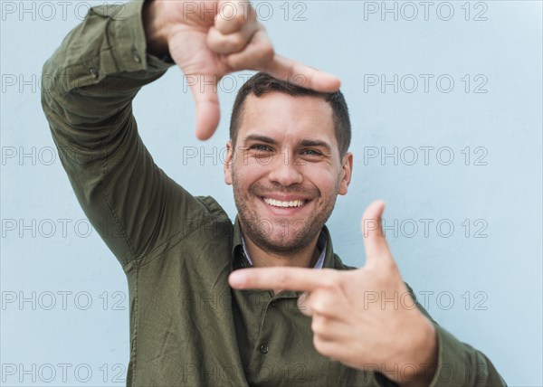 Smiling young man making hand frame blue background