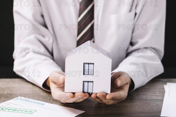 Crop man holding paper house