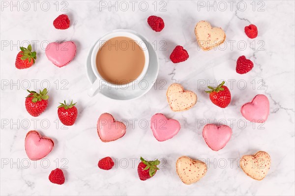 Pink and beige heart shaped French macaron sweets next to coffee cup and strawberry fruits