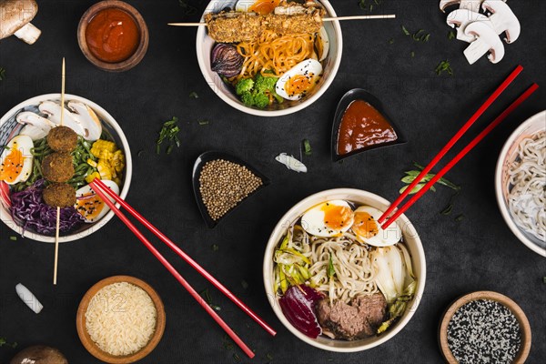 Different type asian style ramen noodles with sauce rice sesame seeds black textured backdrop