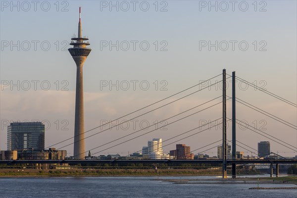 Rheinturm and Rheinkniebruecke illuminated by the setting sun and behind them Neuer Zollhof and Gehry buildings