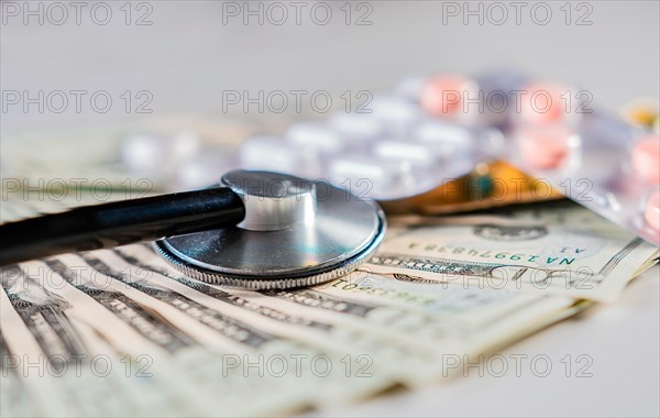 Close up of stethoscope with pills on dollar bills. High cost of medical health with stethoscope. Stethoscope with medicines on dollar bills