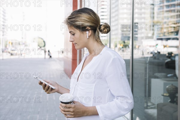 Blonde young woman holding smart phone takeaway coffee cup hands