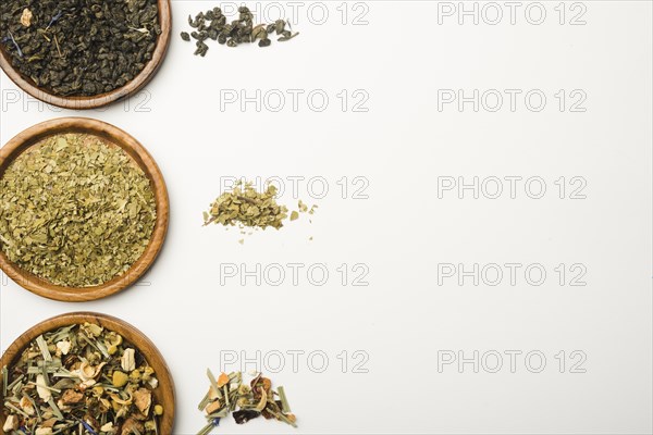 Various dried herbs wooden plates against white background