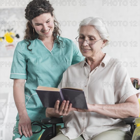 Nurse standing disabled senior woman reading book