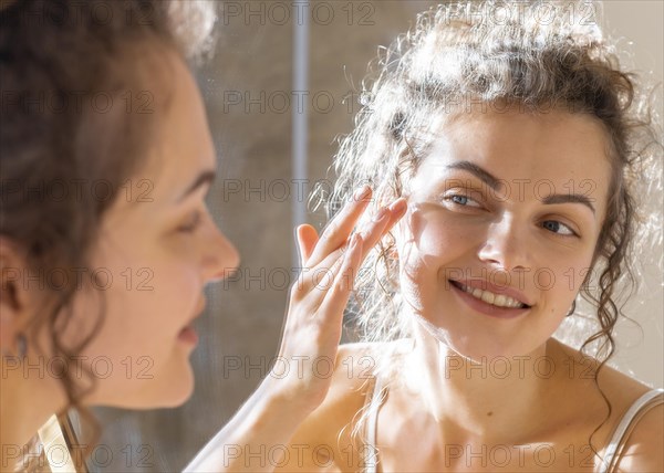 Woman looking mirror applying face cream