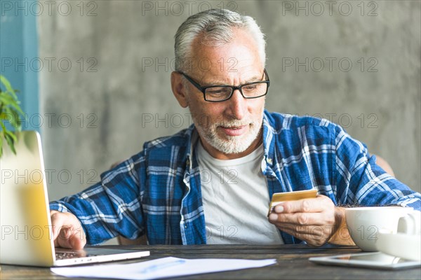 Senior man reading credit card number while working laptop