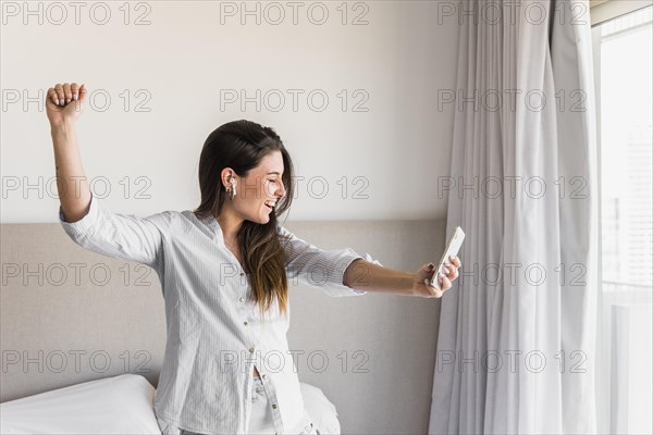Smiling portrait young woman holding mobile phone hand dancing