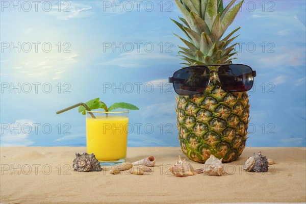 Natural pineapple with sunglasses on the sand of the beach with orange juice