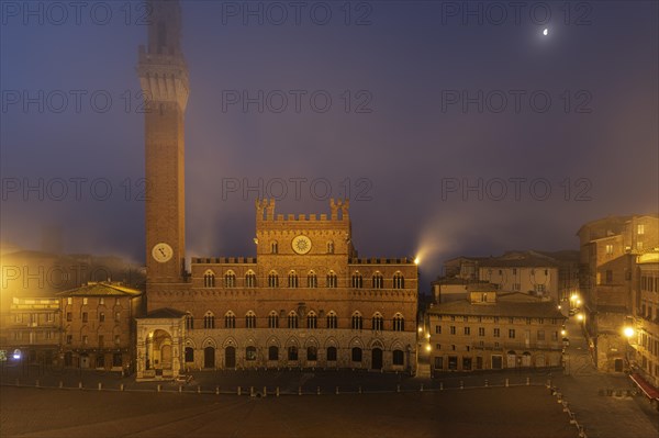 Fog at dawn over the illuminated Piazza del Campo with the bell tower Torre del Mangia and the town hall Palazzo Pubblico