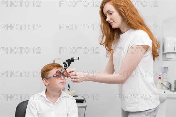 Female ophthalmologist examining boy eyes with optometrist trial frame