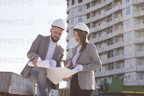 Two architects holding blueprint discussing project while working together