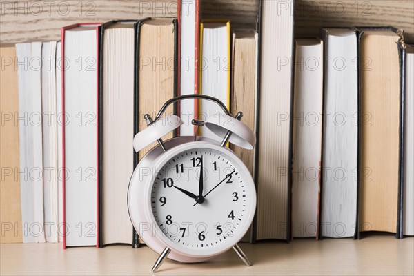White alarm clock showing 10 o clock front bookshelf wooden desk