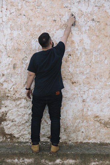 Graffiti artist painting with spray can dirty wall