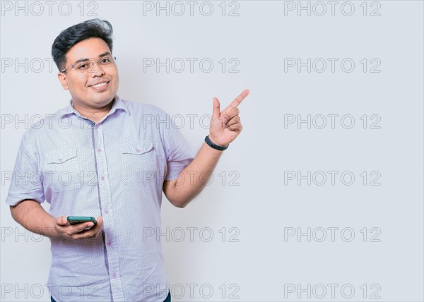 Young latin man holding cellphone pointing to side isolated. Happy guy holding cellphone pointing to the side isolated