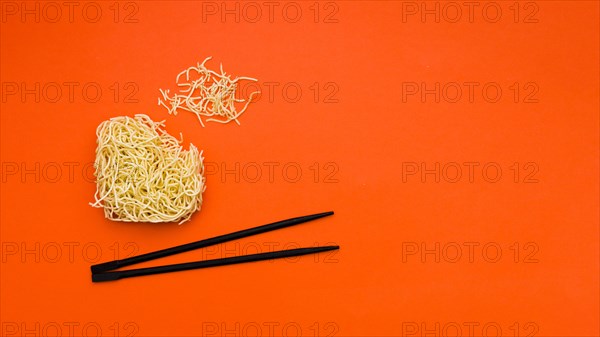 Broken dry instant noodles with chopsticks orange background