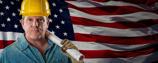 Male contractor wearing blank yellow hardhat over waving american flag background banner