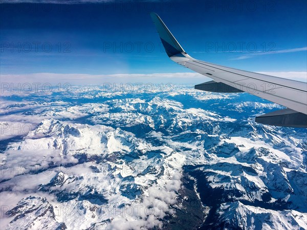 View from aeroplane window bird's eye view aeroplane jet holiday plane wide-bodied aeroplane on snow-covered alpine high mountains in front of snowmelt of Swiss Alps