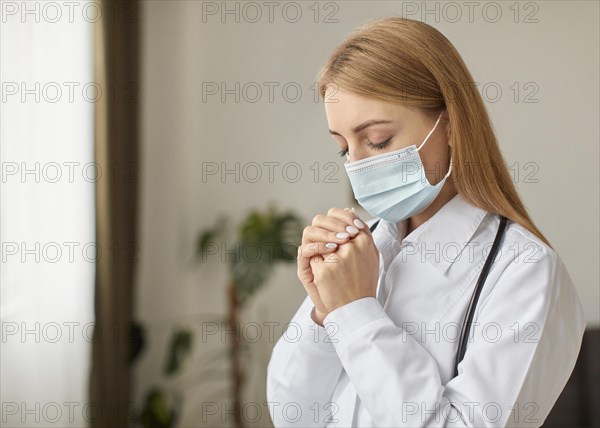 Side view covid recovery center female doctor with stethoscope medical mask praying