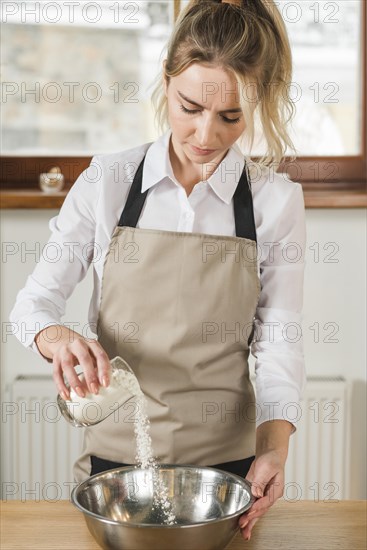 Young woman pouring flour from glass mixing stainless steel bowl