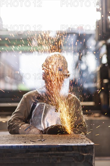 A worker grinds on a slab in a steel mill