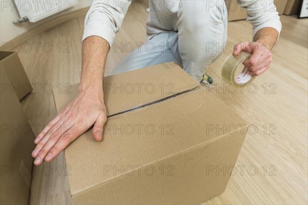 Close up male sealing cardboard box with adhesive tape