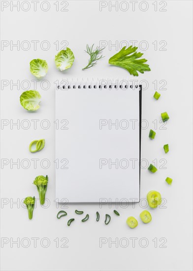 Varieties chopped vegetables surrounding spiral notepad white backdrop