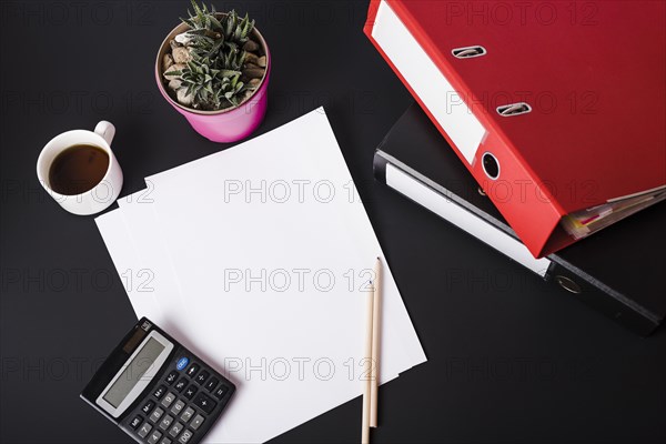 Overhead view coffee cup calculator pot plant blank white papers pencils paper files black background