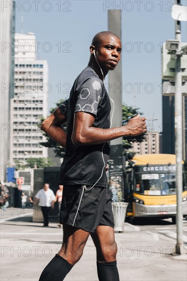 Confident male athlete fit young man jogging road listening music earphone