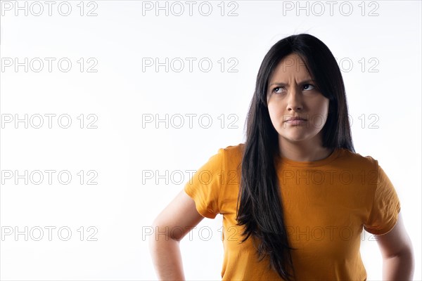 Young latin woman frowns and looks up to the left. Studio portrait on white background. Horizontal format