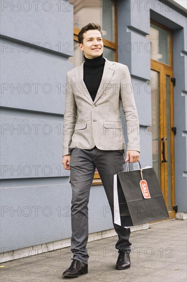 Fashionable young man holding shopping bag with sale tag