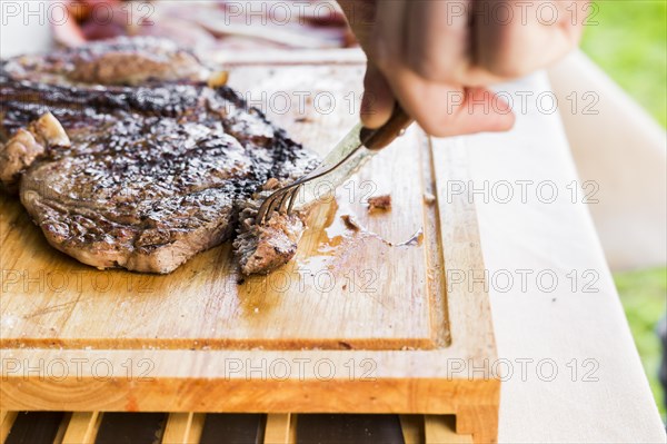 Person s hand holding knife fork cutting grilled beef steak chopping board