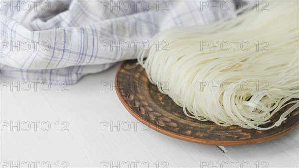 Dried rice vermicelli noodles circular plate near checkered cloth white surface
