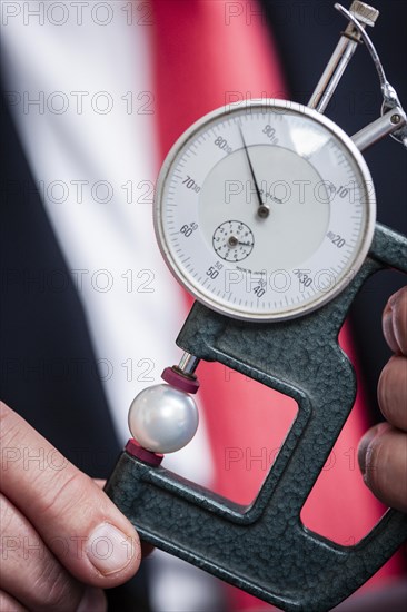 An appraiser with a measuring device device to determine the diameter of a white pearl