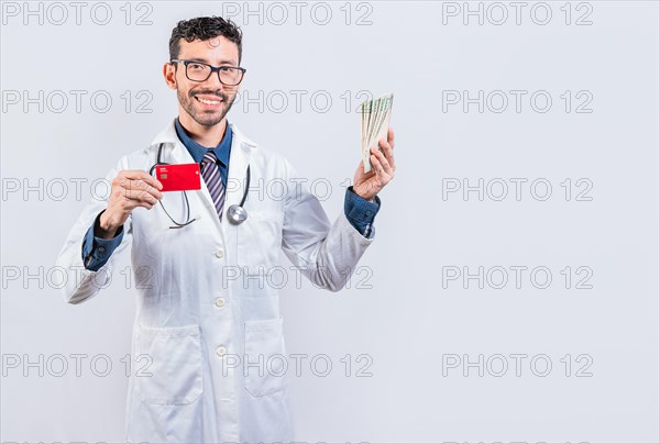 Handsome doctor holding money and credit cards isolated. Happy young doctor holding credit card and money isolated