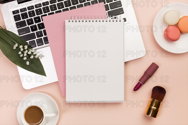 Spiral notepad laptop with macaroons coffee cup with makeup brushes colored backdrop