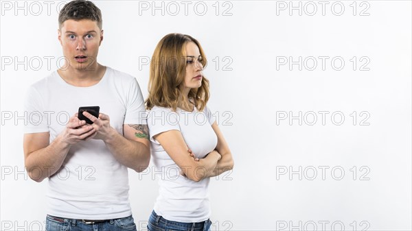 Shocked man holding mobile phone hand standing near her angry girlfriend