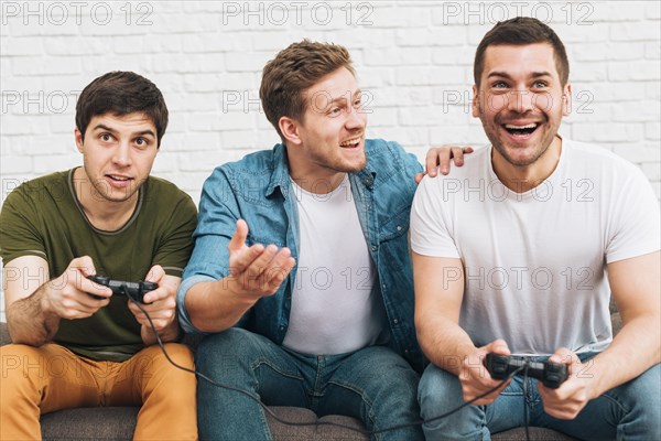 Three male friends sitting together enjoying video game