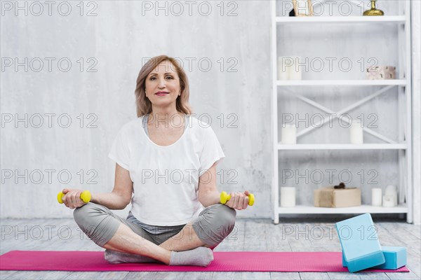 Portrait beautiful woman sitting yoga mat near blocks holding yellow dumbbells home