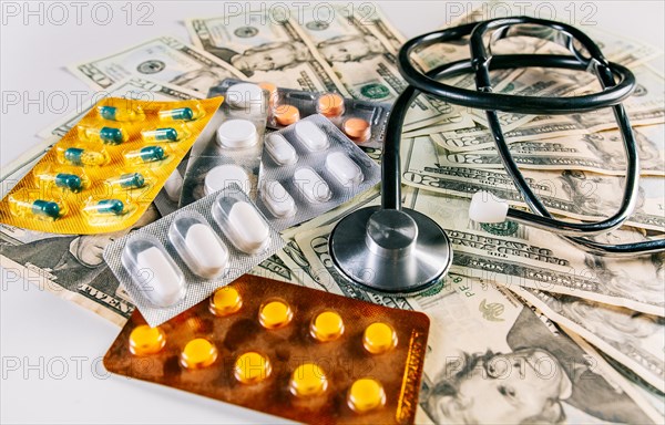 Stethoscope with pills on money isolated. High cost of medical health with stethoscope. Medical stethoscope with medicaments on money