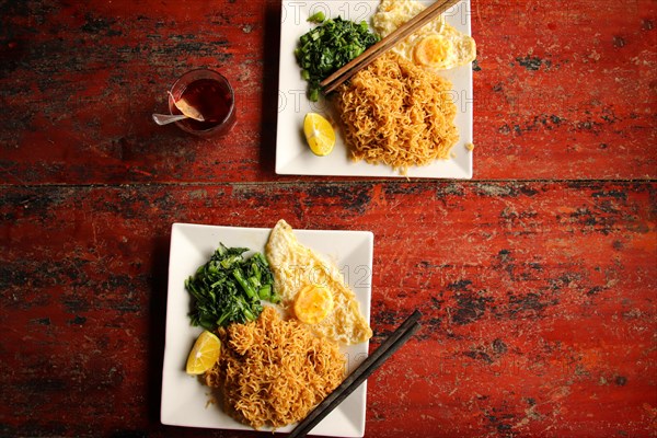 Stir fried wonton noodles with fried egg and spinach against a rustic red table