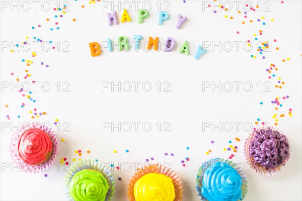 Happy birthday text with colorful muffins white backdrop