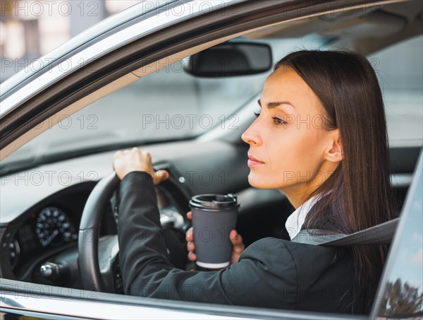 Young businesswoman holding disposable coffee cup driving car