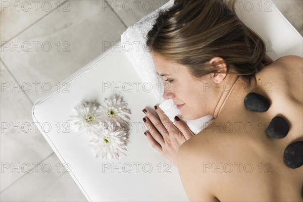 High angle view young woman lying bed receiving hot stone massage