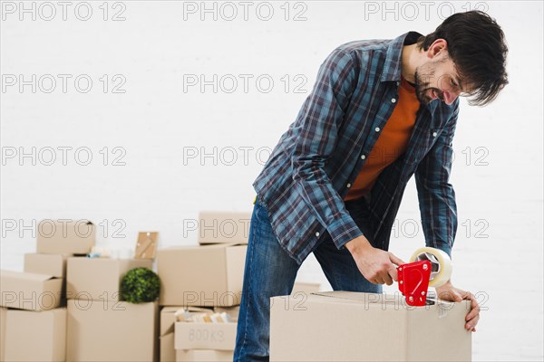 Smiling portrait young man sealing cardboard box with duct tape