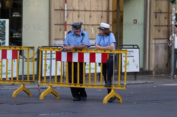 Policeman and policewoman leaning against bars of a road barrier